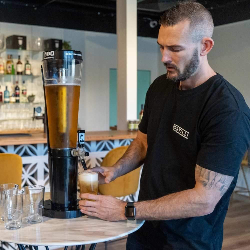 
                  
                    A bar worker is pouring a beer from a booze towers beer tower that is sitting on the middle of a table in a bar
                  
                